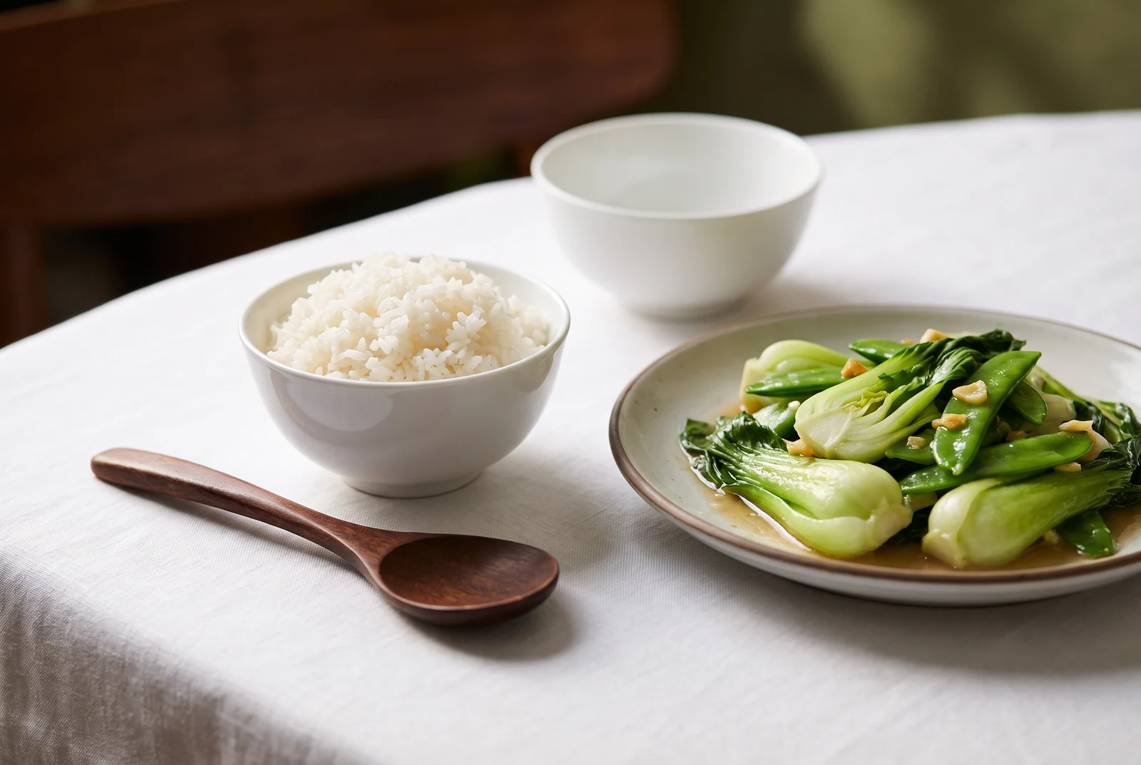 Small bowl of rice beside a plate of leafy green vegetables
