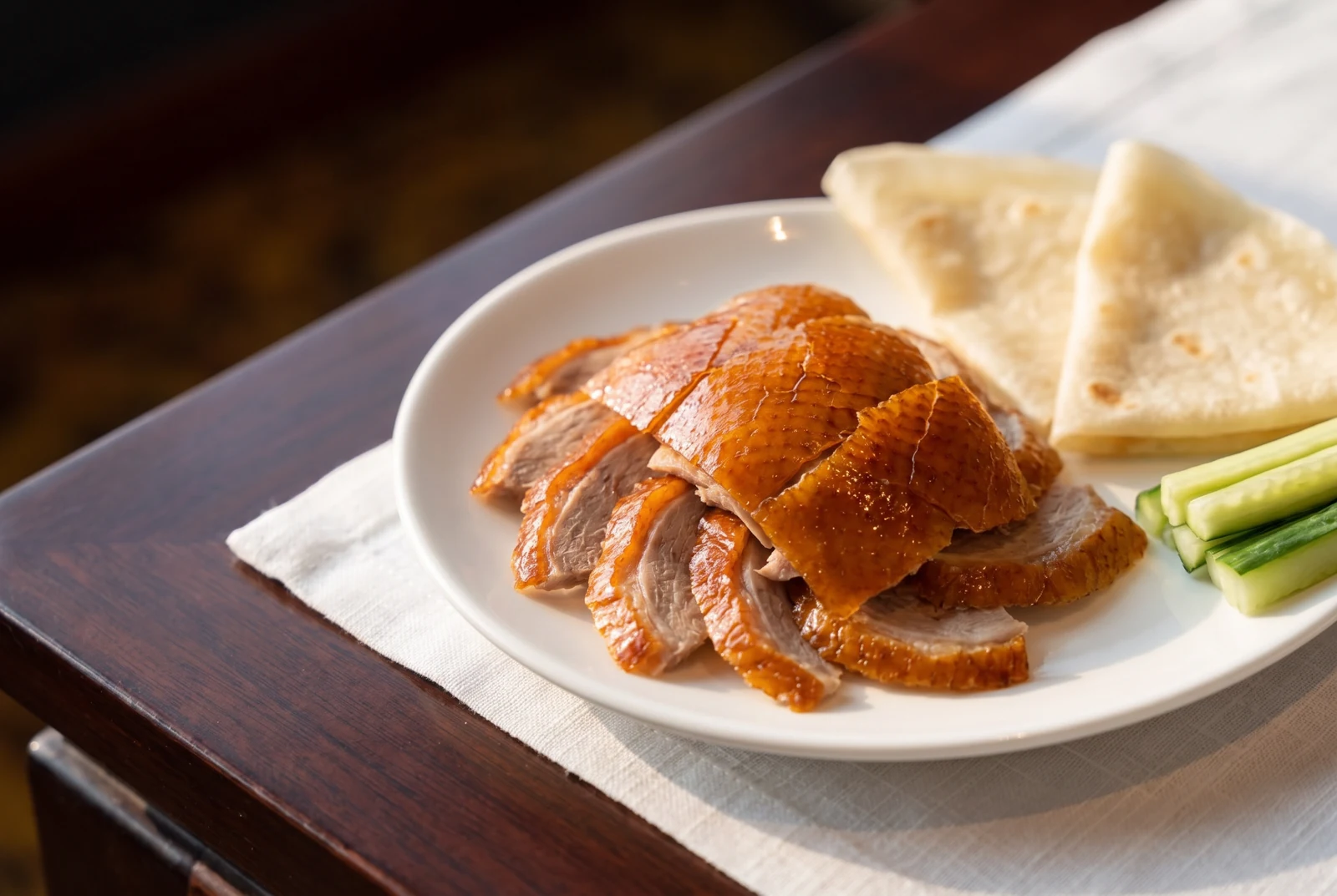 Thin slices of duck with pancakes and cucumber on a white plate